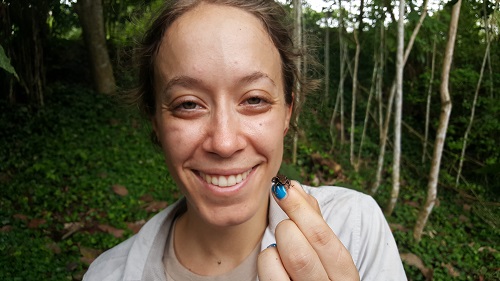 Rebecca Tarvin smiling and holding up a very small frog